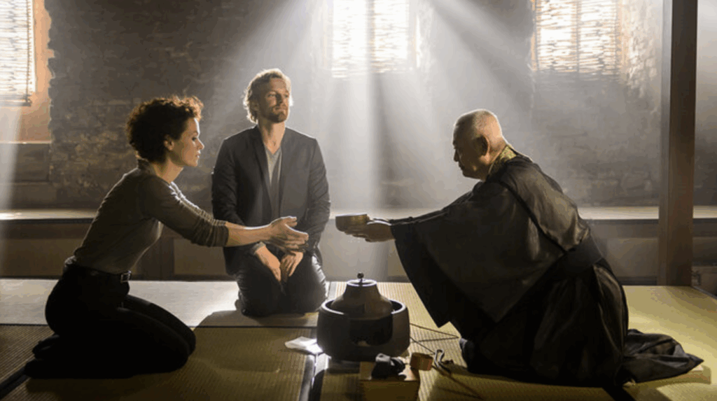 a monk hands overs a bowl to Louise